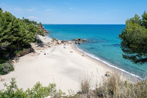 A beach with clear blue water, sandy shore, and rocky outcrops.
