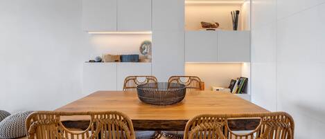 Un comedor con mesa de madera, sillas de mimbre y estanterías empotradas decoradas con objetos ornamentales.