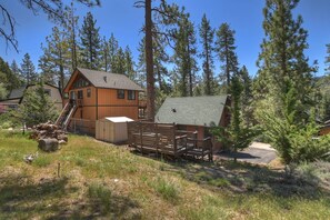 A cabin with a wooden exterior, a covered porch, and a surrounding forest. - Knotty By Nature By Destination Big Bear: Modern Cabin Decor! Spa! Pet Friendly! Close to Bear Mountain Ski Resort! (Big Bear Lake)