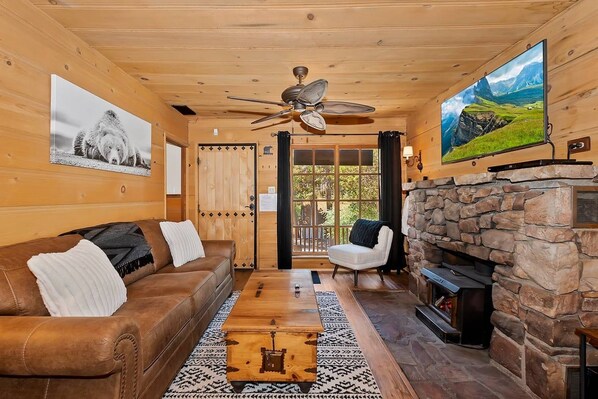 A cozy living room with a stone fireplace, leather sofa, and a television mounted on the wall.