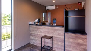 A modern hotel reception area with a digital check-in station, air conditioning units, and a view of the outdoors through a large window. - HOTEL R9 The Yard Izumi (Izumi)