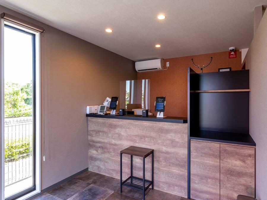 A modern hotel reception area with a digital check-in station, air conditioning units, and a view of the outdoors through a large window.