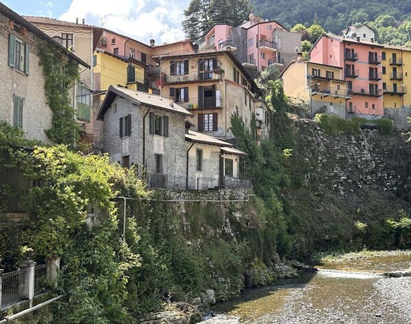 A hillside residential area with buildings in various colors, a river running through, and a stone bridge.