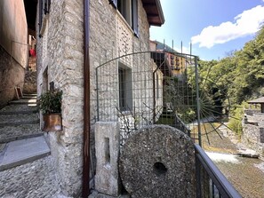 A stone building with a metal gate, a stone well, and a river in the background.