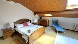 Ein Schlafzimmer mit Holzboden, einem Bett, einem Sessel, einem Nachttisch und einem Fenster.