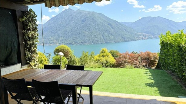 Ein Außenbereich mit Tisch und Stühlen, Blick auf einen See und Berge im Hintergrund.