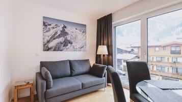 Een moderne woonkamer met een grijze bank, een glazen salontafel en uitzicht op een berglandschap door grote ramen.