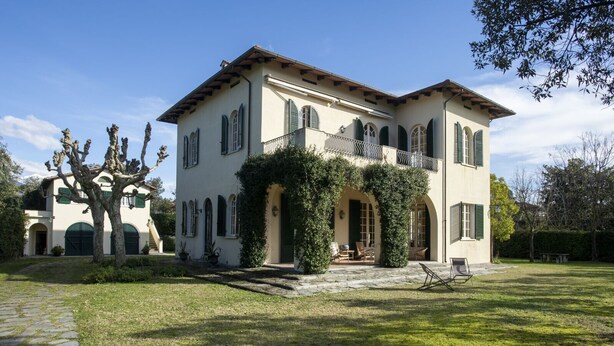 A two-story house with a stone pathway leading to the entrance, surrounded by a well-maintained lawn and a large tree.