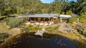 Une maison moderne dotée d’un patio couvert, d’un étang orné de nénuphars et bordée d’une forêt.