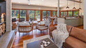 Un vaste espace de vie doté d’un plancher en bois, d’un canapé en cuir marron et d’une table à manger avec des chaises. On y trouve également une cuisine équipée d’un évier et de placards, ainsi que de grandes fenêtres offrant une vue sur l’extérieur.