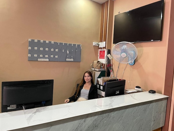 Un comptoir d’accueil équipé d’un téléviseur à écran plat, d’un ventilateur fixé au mur et d’un panneau d’affichage indiquant les numéros des chambres.