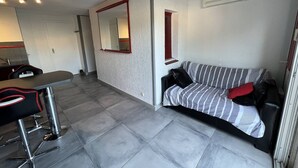 A modern, compact living space with a kitchenette, a striped sofa, and a dining area with a bar stool. - T2 Cabin with Air Conditioning - Sleeps 4 (Port Leucate)