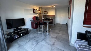 A compact living space with a kitchenette, a dining area with bar stools, a flat-screen TV, and a bed. - T2 Cabin with Air Conditioning - Sleeps 4 (Port Leucate)