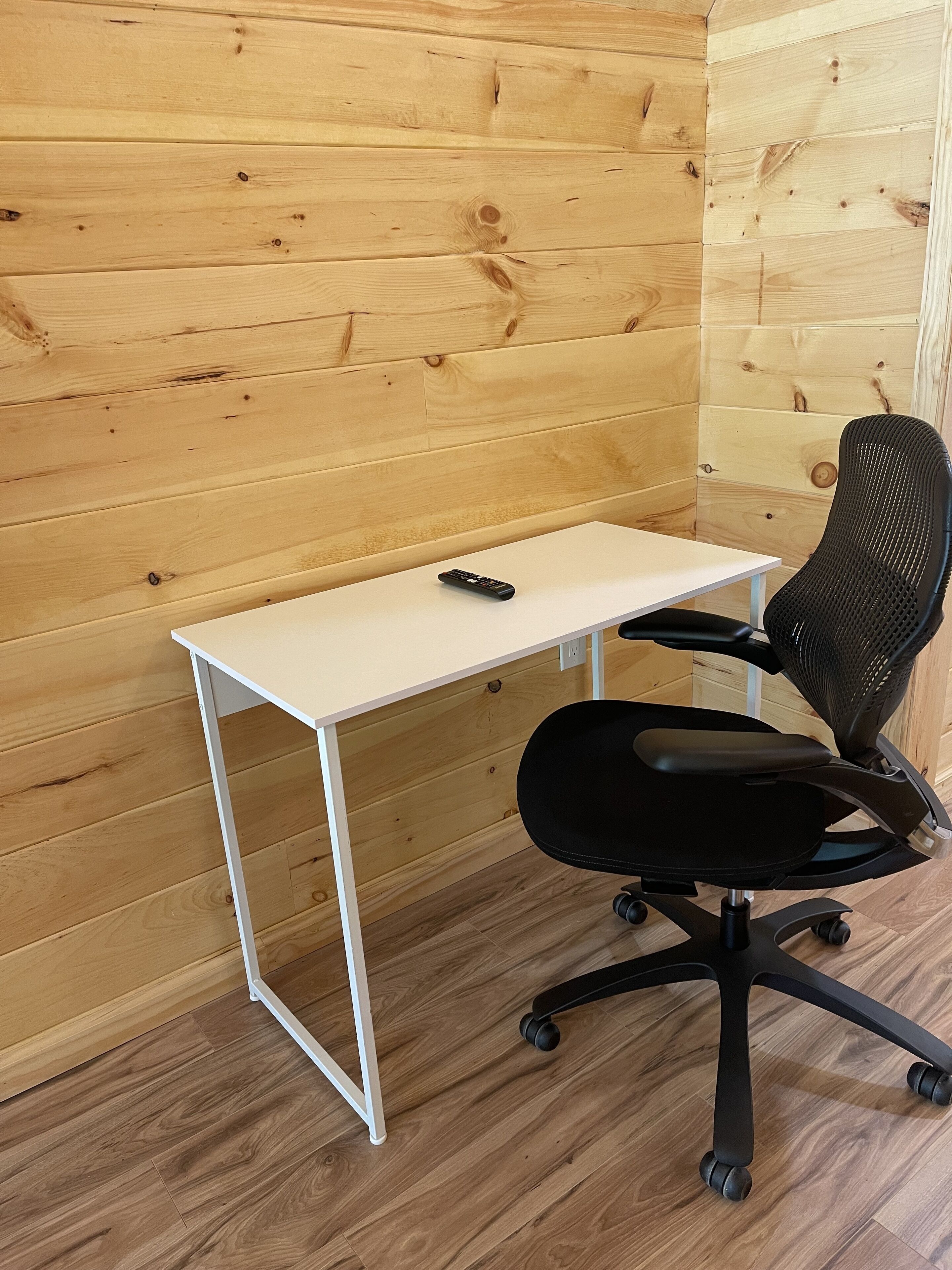 A wooden-paneled room with a white desk and a black office chair.