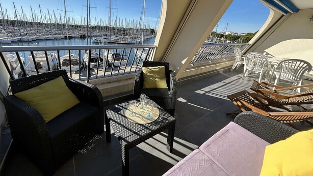 A balcony with wicker furniture, a table with glasses, and a view of a marina with boats. - Air-conditioned Apartment 6 pax with Terrace and Pool in Port Camargue (Port Camargue)