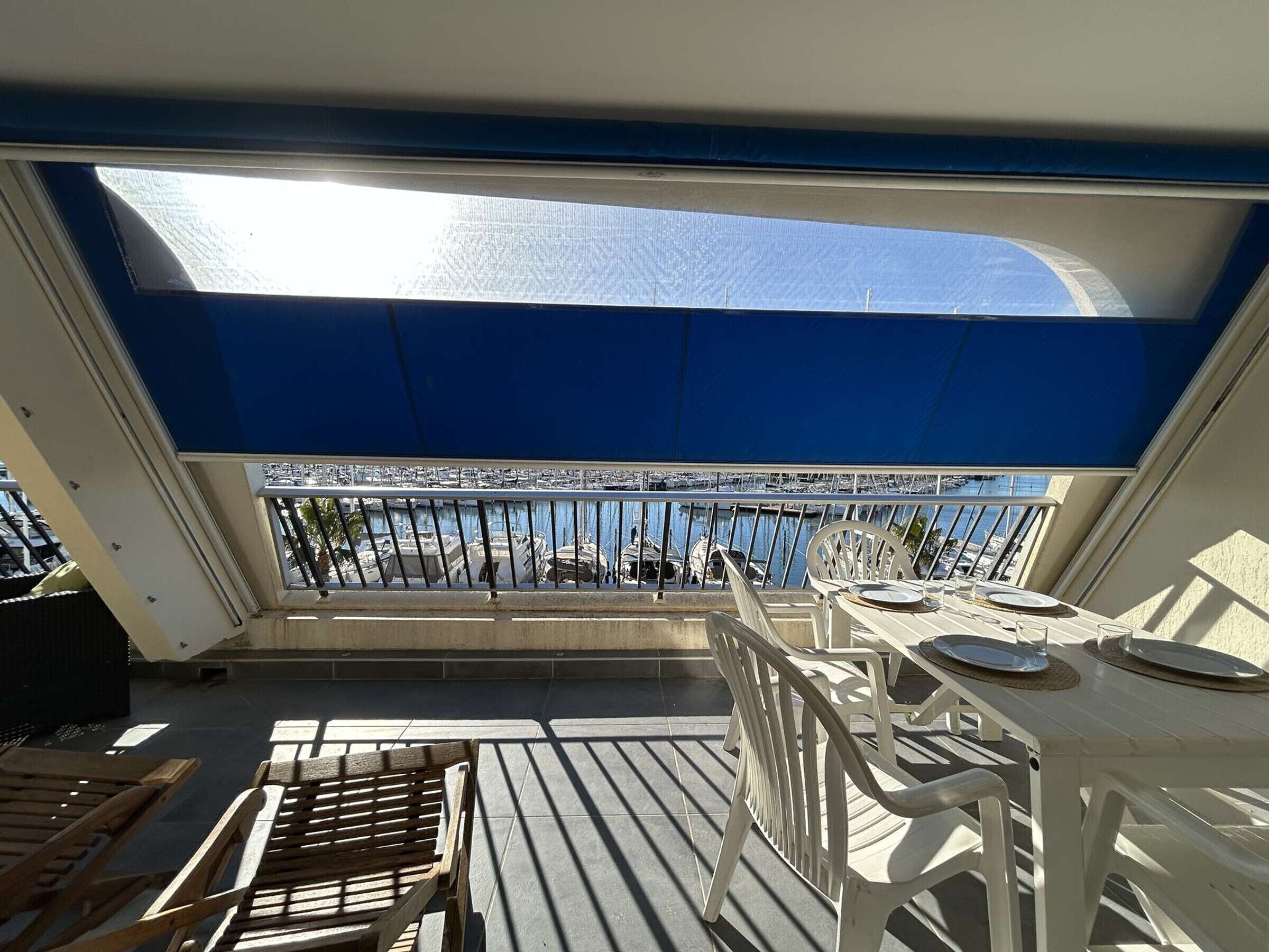 Un balcón con mesa lista para comer, con vista a un puerto deportivo y barcos.