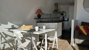 A modern kitchen with white cabinetry, a microwave, and a gas stove. There is a dining area with a white table and chairs, and a sofa with cushions in the living room. - Air-conditioned Apartment 6 pax with Terrace and Pool in Port Camargue (Port Camargue)