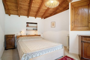 Une chambre avec un plafond en bois, un lit avec une literie à motifs, une table de chevet, une commode et un radiateur.