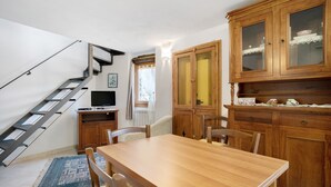 Un comedor con una mesa y sillas de madera, una escalera y armarios de madera con puertas de vidrio.