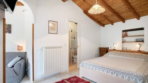 Un dormitorio con cama, sofá, radiador, techo de madera y un pasillo que lleva a un baño.