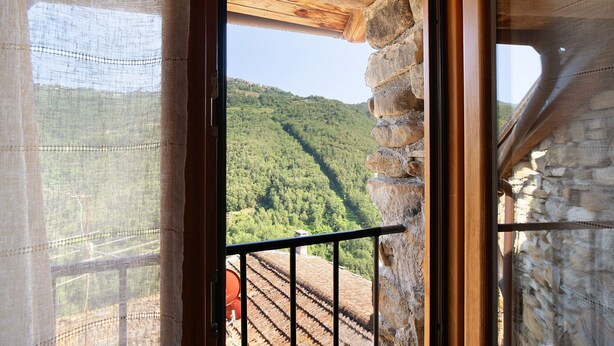 Una habitación con pared de piedra, techo de madera y vista a una ladera boscosa.