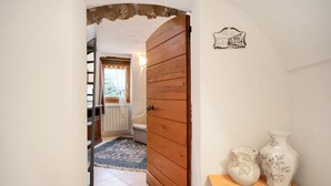 Un pasillo con una puerta de madera, un radiador, un tapete estampado y dos jarrones sobre una mesa de madera.