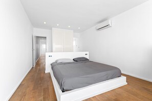 A modern bedroom with a white bed, grey bedding, wooden flooring, and a white wardrobe.