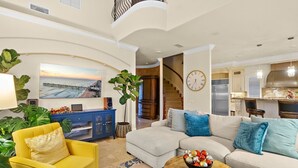 A spacious living room with a large sofa, a yellow armchair, and a coffee table. A staircase leads to an upper level, and a kitchen is visible in the background.