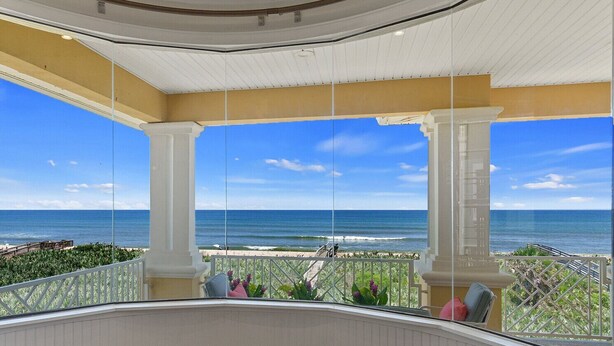 A balcony with a view of the ocean, white columns, and a railing.