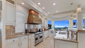 A spacious kitchen with white cabinetry, granite countertops, and a large island with a sink.