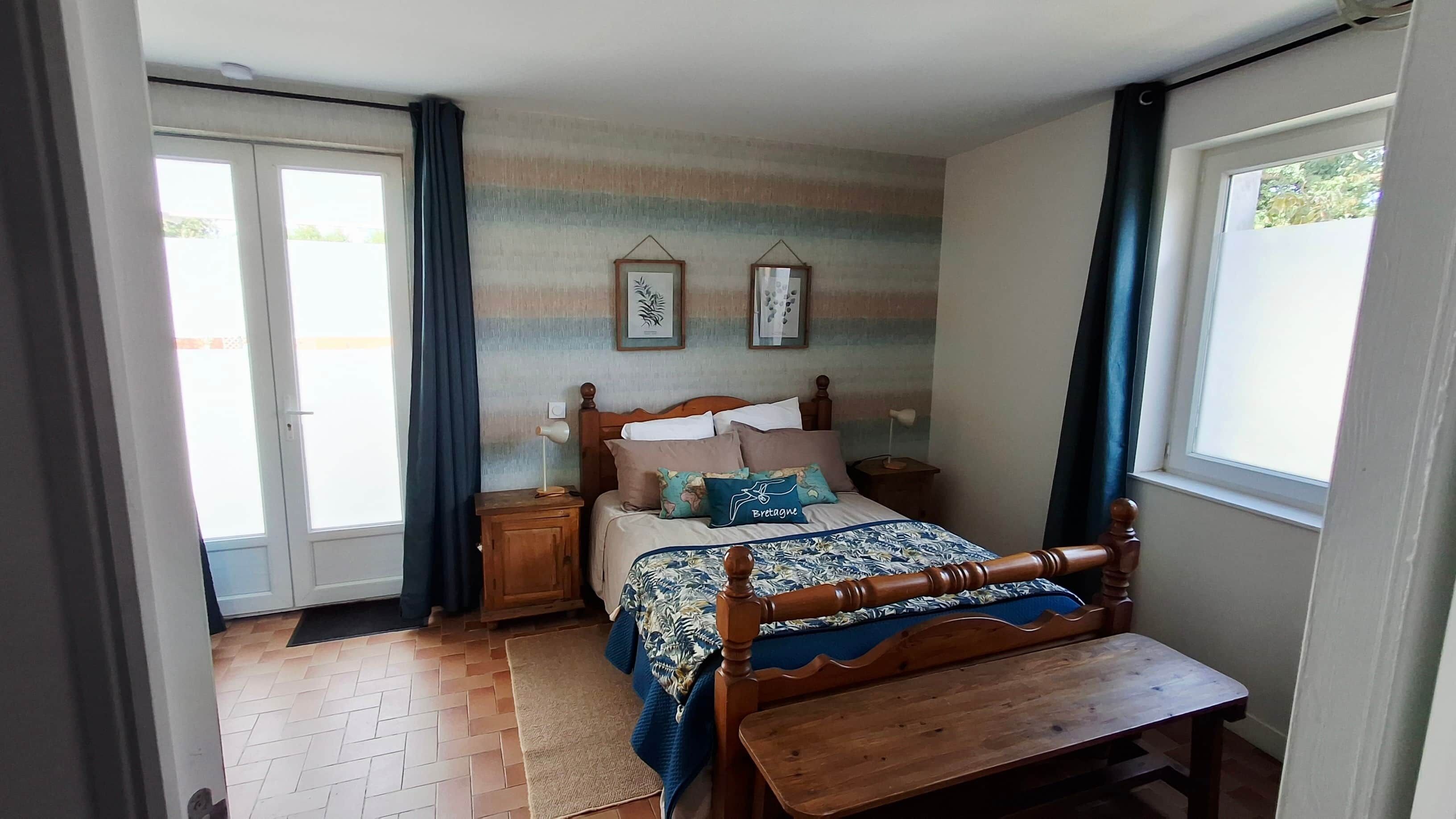 Een slaapkamer met een bed, nachtkastjes, een houten bankje, een raam en een deur.