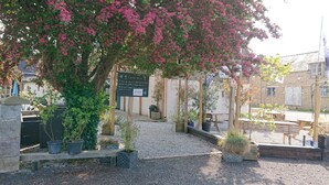 A courtyard with a pergola covered in pink flowers, a signboard, and a gravel path. - Le Black Dog Pub Bedroom  5 (Saint-Aignan)