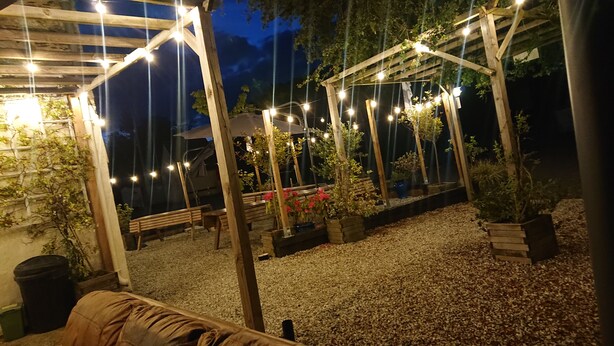 An outdoor patio area with wooden pergolas, string lights, and potted plants. - Le Black Dog Pub Bedroom  5 (Saint-Aignan)