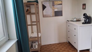 A small, clean room with a white dresser, a wooden shelf with towels, a coffee maker, and abstract art on the wall. - Le Black Dog Pub Bedroom  5 (Saint-Aignan)