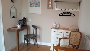 Une petite pièce, bien rangée, avec un bureau, deux chaises, un radiateur, un miroir et une étagère contenant divers objets.