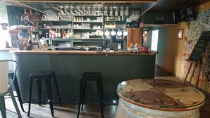 Un espace bar avec des tabourets, un tonneau en bois, et une variété de bouteilles et de verres disposés sur des étagères.