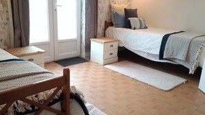 Une chambre avec deux lits, une chaise en bois, une petite table de chevet et une porte avec un rideau.