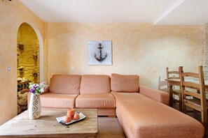 A living room with a sofa, a wooden coffee table with a vase and fruit, and a painting of an anchor on the wall.