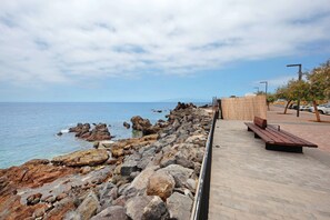 A rocky shoreline with a paved walkway, benches, and a view of the sea.
