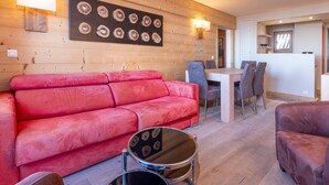 A cozy living area with a red sofa, a dining table with chairs, and a wall decorated with circular wooden pieces. - 3-room flat, 6 ppl, Southwest balcony, near slopes (Avoriaz)