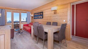 A wooden-paneled room with a dining table and chairs, a red sofa, and a wall-mounted light fixture. - 3-room flat, 6 ppl, Southwest balcony, near slopes (Avoriaz)