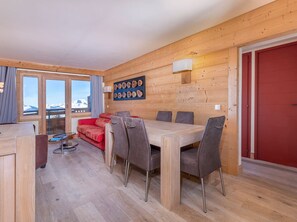 A wooden-paneled room with a dining table and chairs, a red sofa, and a wall-mounted light fixture. - 3-room flat, 6 ppl, Southwest balcony, near slopes (Avoriaz)