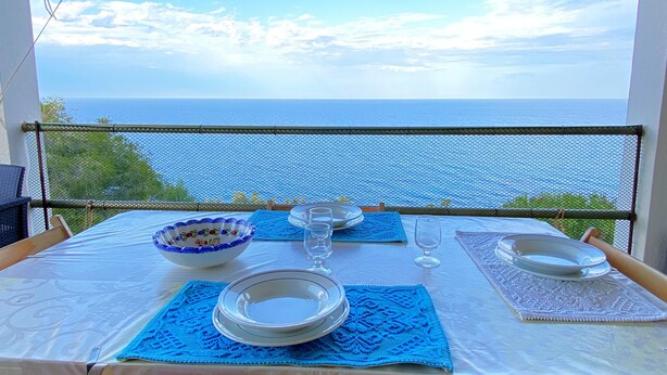 Una mesa lista para comer con vista al mar, barandilla de malla y techo blanco.