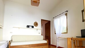 Una habitación con sofá de madera, una mesita pequeña, lámpara colgante, ventana con cortinas y una puerta.
