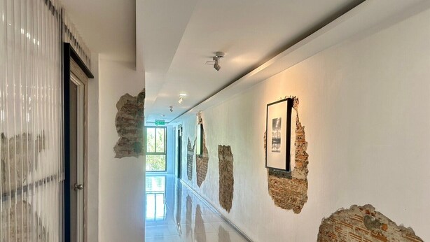 Un pasillo de diseño moderno, con una puerta de cristal a la izquierda y una serie de cuadros enmarcados en la pared derecha.