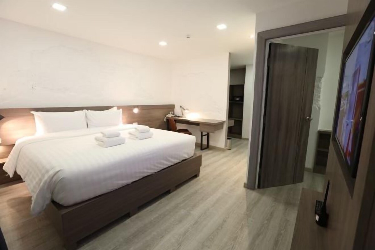 A modern hotel room with a large bed, a bedside table, and a desk.