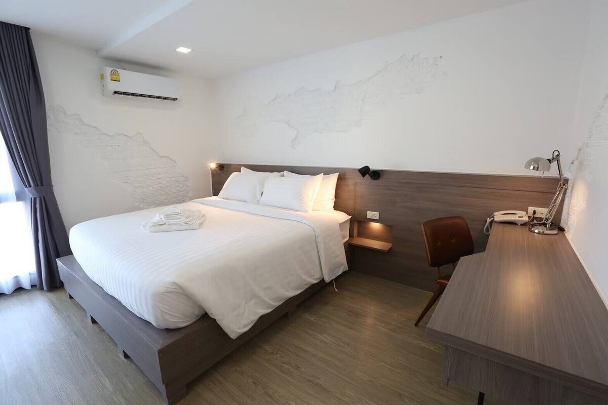 Ein Hotelzimmer mit einem großen Bett, einem Schreibtisch, einem Sessel, einem Nachttisch und einer Wand-Klimaanlage.