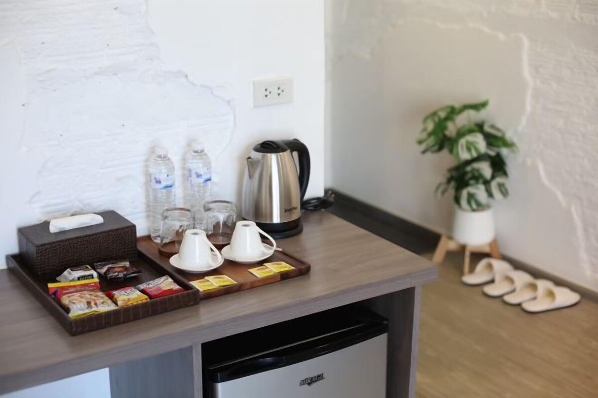 A hotel room's reception area with a coffee station, a kettle, and a plant.