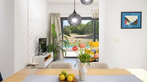 Una sala de estar moderna con una mesa de comedor, un florero con flores y vistas a un jardín a través de grandes ventanales.