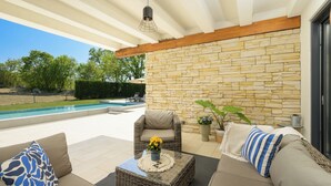 Un área de estar al aire libre con techo, una pared de piedra, una piscina y mobiliario exterior.
